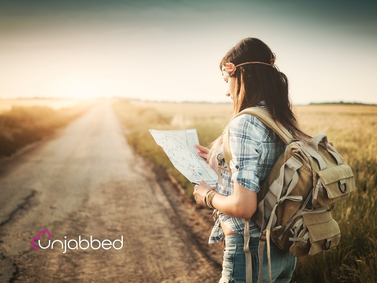 A woman standing on a long and lonely road out in the middle of nowhere looking at a map. It is symbolic of navigating the world of unvaccinated dating.