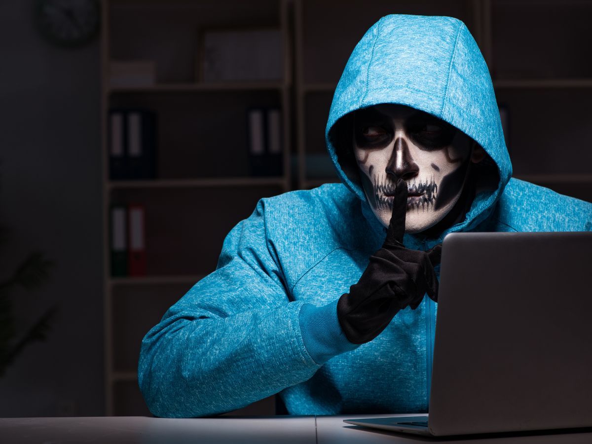 A hacker in a blue hoodie wearing a skull mask